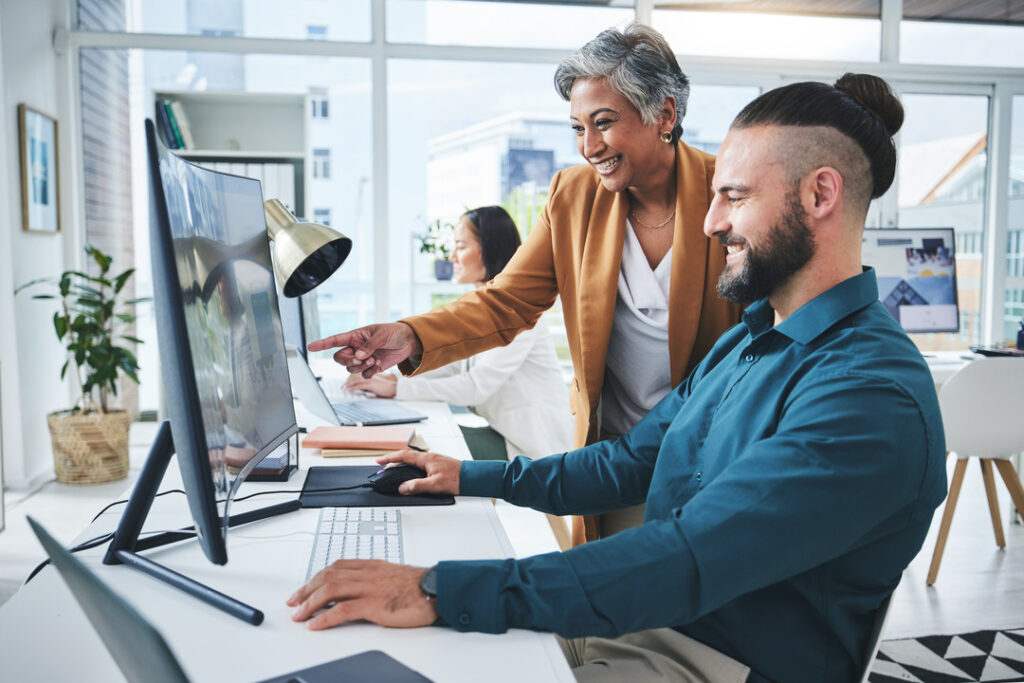 A manager helping an employee in an office at his computer