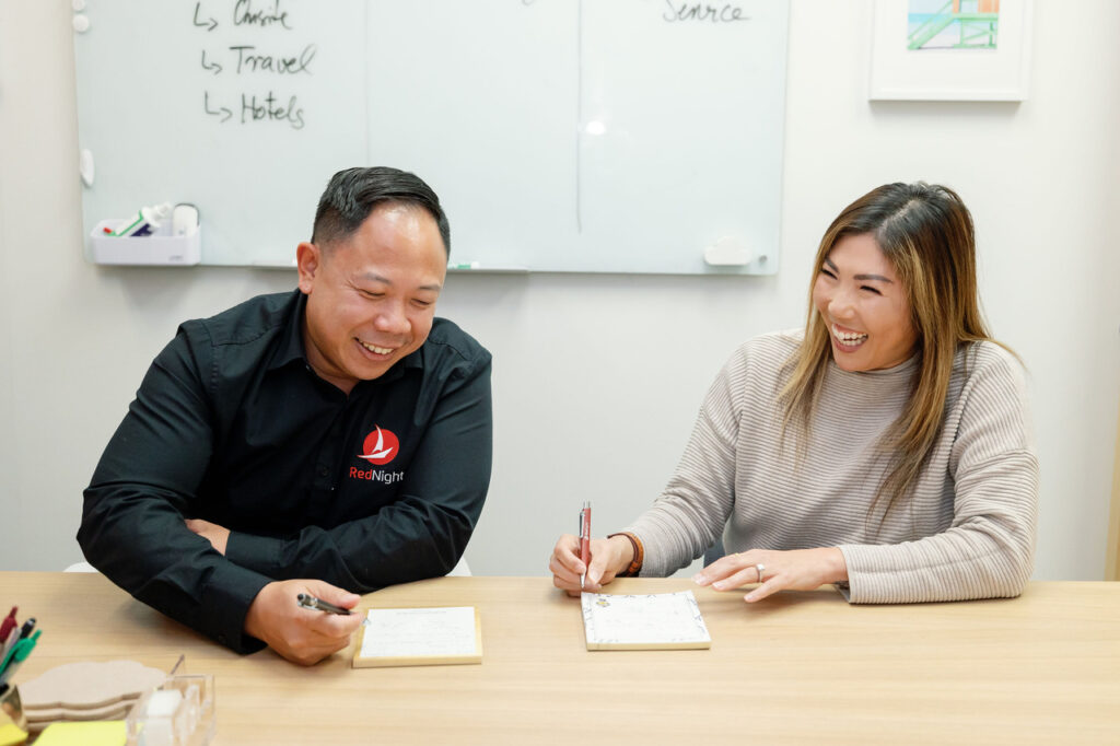 Two professionals sit at a table at write in notepads