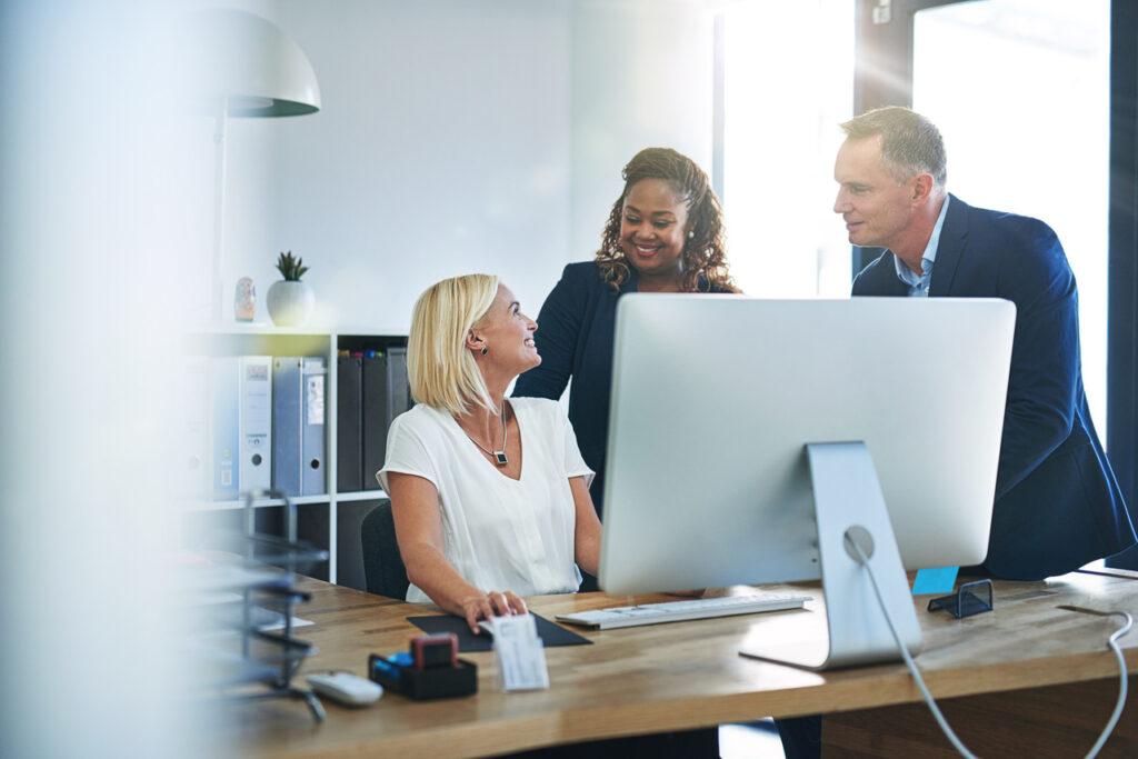 Woman on a computer smiling at two other employees